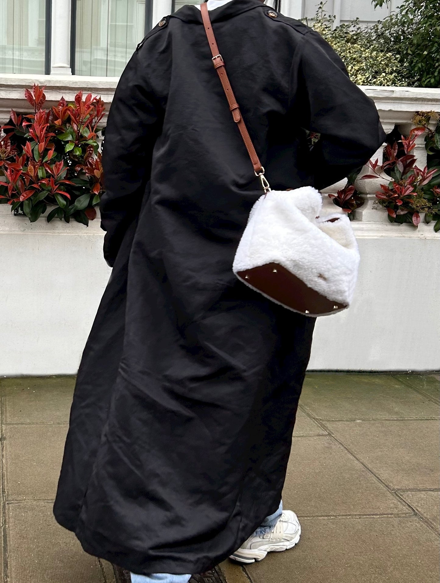 Our Celia bag, a white shearling handbag mixed with brown leather for the handle and base of the bag, worn as a crossbody bag in the photo outdoors.