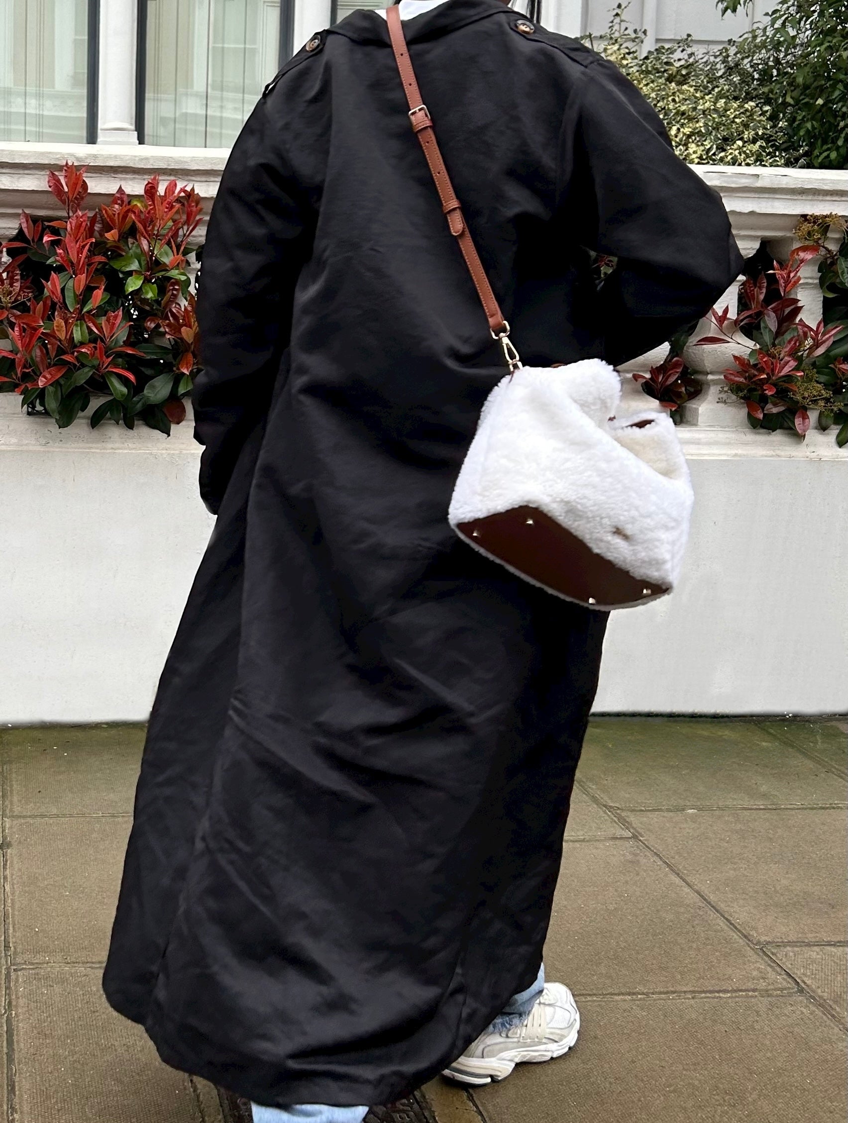 Our Celia bag, a white shearling handbag mixed with brown leather for the handle and base of the bag, worn as a crossbody bag in the photo outdoors.