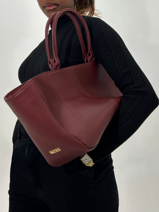 Model carrying our Burgundy leather tote bag, the Colette Tote, showcasing our signature 'KEEKS' logo on the side of the bag in gold metal hardware. 